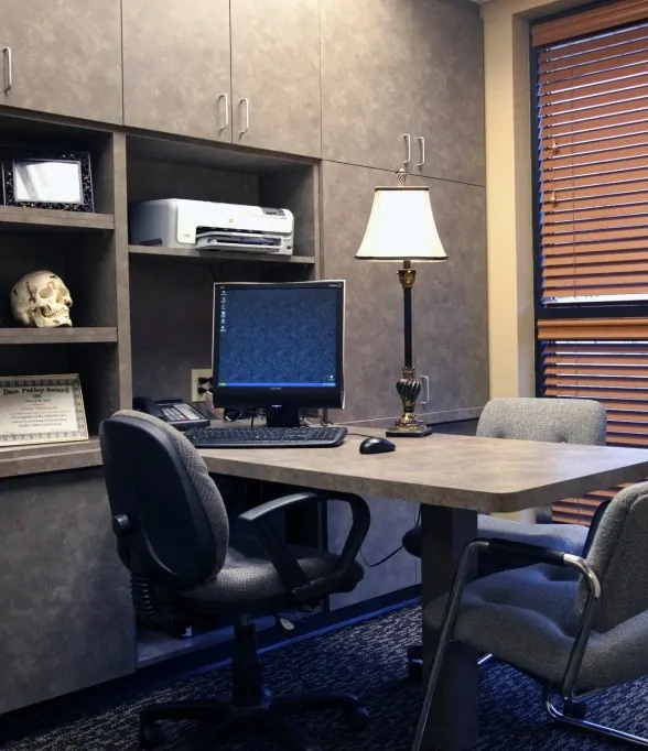 A consultation office with a desk, computer, lamp and a model skull on the shelf.