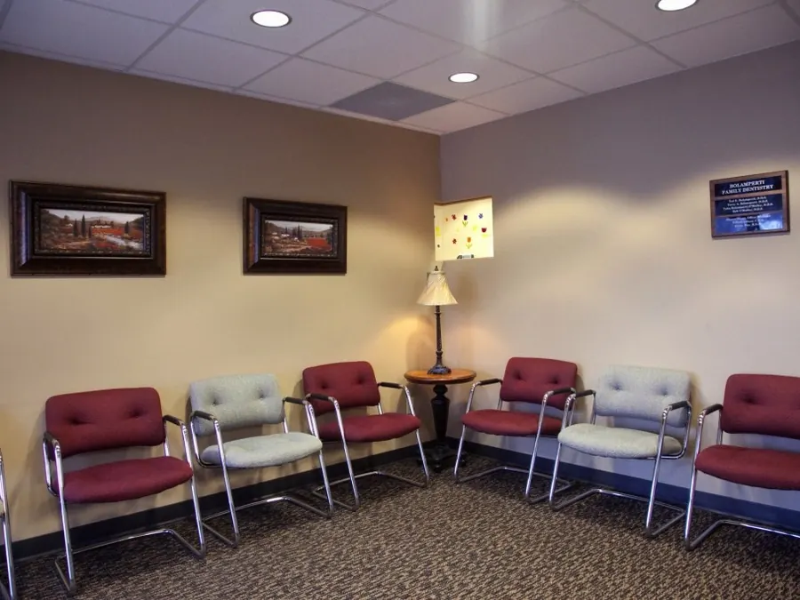 The waiting room, with red and grey chairs, framed paintings and a table lamp.